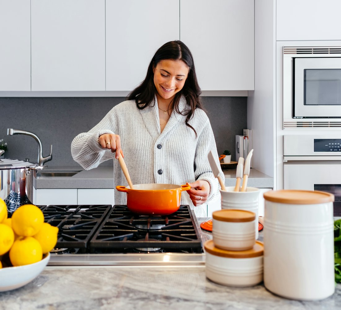 A home cook stirring a pot on the stove in her own kitchen